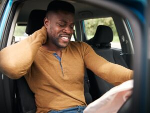 man holding the back of his neck inside a car