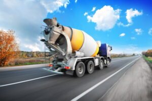 Concrete mixer truck driving fast on the countryside road with trees against blue sky with clouds