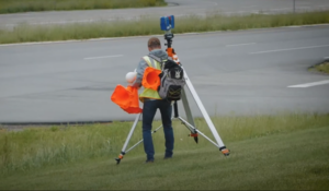 accident reconstructionist carrying gear through a field towards the road