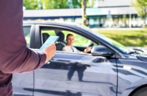 Customer waiting driver to pick up on city street. Man holding smartphone. Mobile and online booking for rideshare transportation with cellphone.
