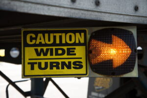 18-Wheeler Caution Wide Turns Sign with Lighted Arrow. Sign is on the undercarriage of a trailer on a big rig truck.
