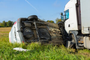 A car lying on its side next to an overturned semi-truck in a field